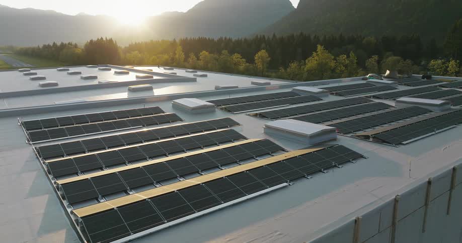 The sun shines over mountains on to solar panels on the roof of a building