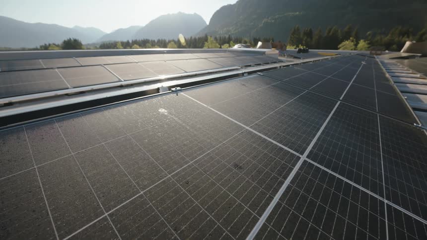 The sun shines brightly upon solar panels and there are trees in the distance