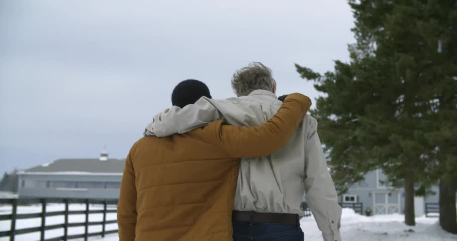 Two people with their arms around each other walk towards a house