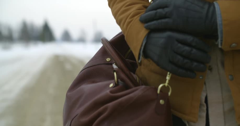 A man in a brown jacket grasps the strap of his bag