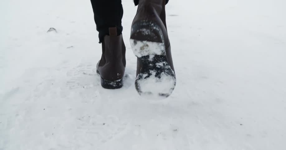 A man walks in the snow wearing leather boots