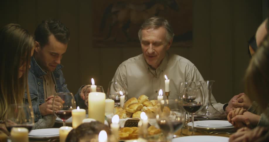 A family is praying at a table filled with food