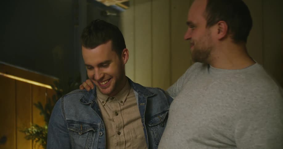 Two men have their arms around each others shoulders and are talking and laughing