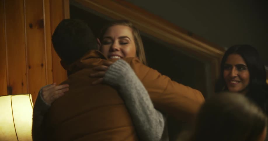 A woman hugs a man inside a house at night