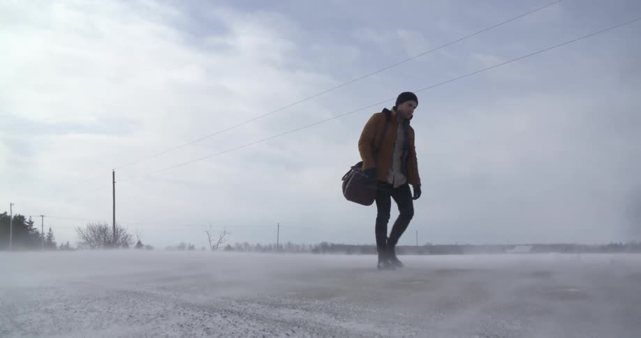 A man walking down a road as snow blows around him