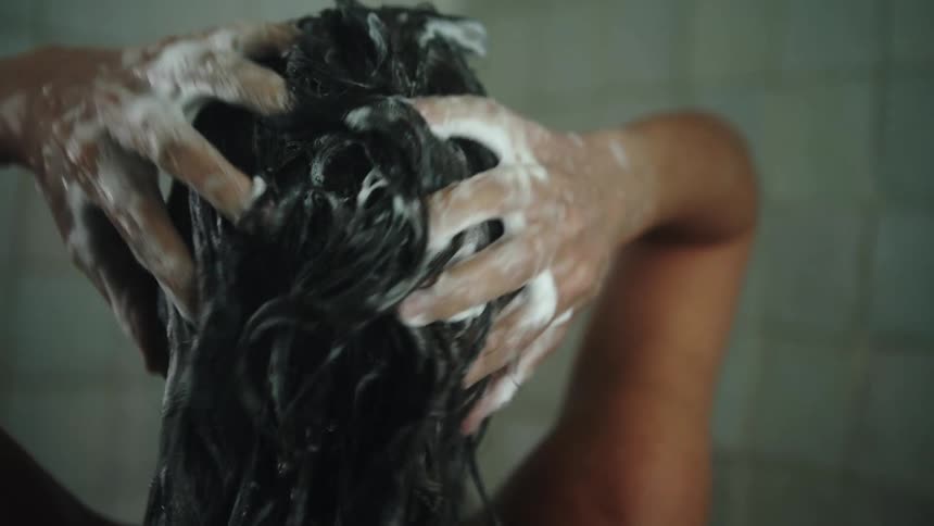 A woman shampoos her long dark hair in the shower
