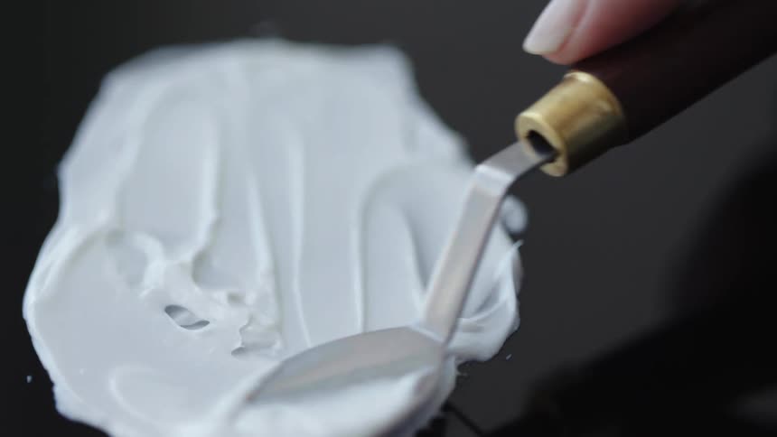 A spoon spreads white lotion onto a dark surface