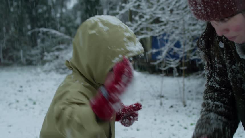 A little boy adds snow to the base of the snowman he and mom are building