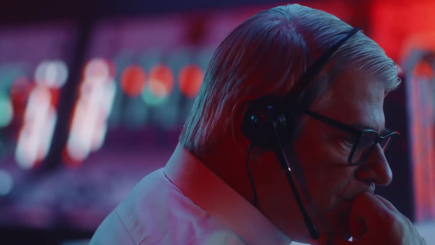 A man is wearing glasses and a headset and there are lights flashing behind him