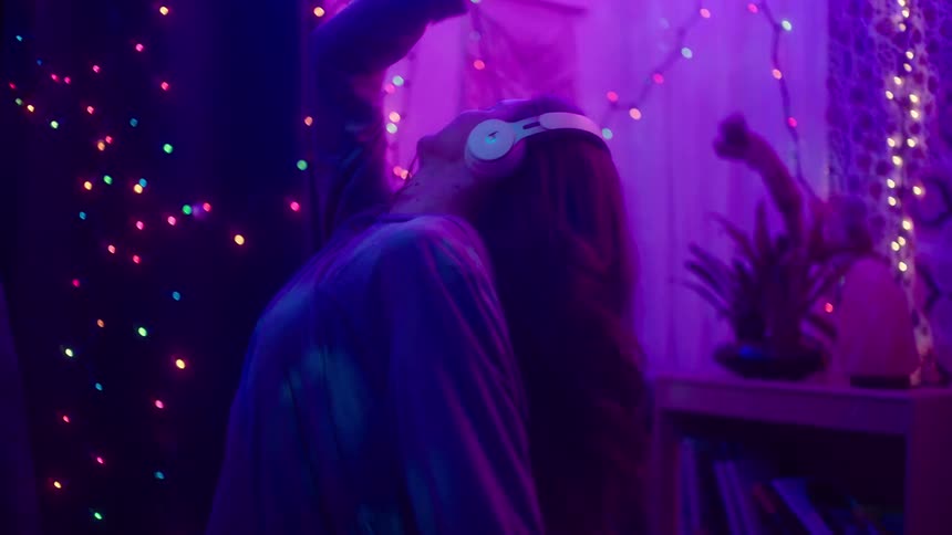 Woman wearing headphones dances in room lit by purple lighting