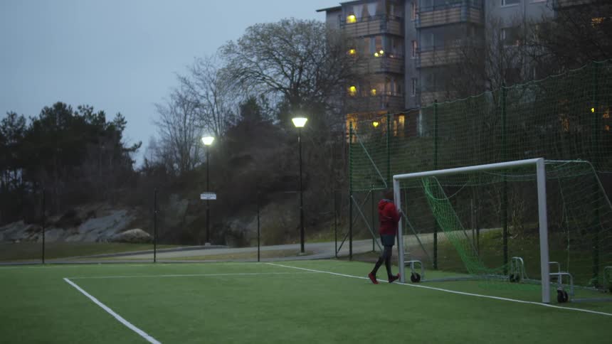 Man uses a soccer goal post to stretch on a soccer field in the morning
