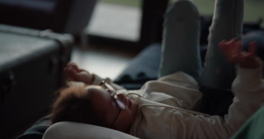 A girl rolls onto the couch while her sister scrolls through her phone