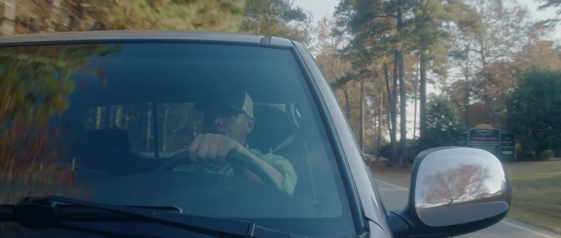 A man driving a truck down a tree lined street