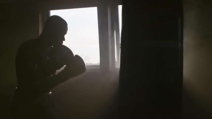 Light shines in windows as a boxer is working out with a punching bag