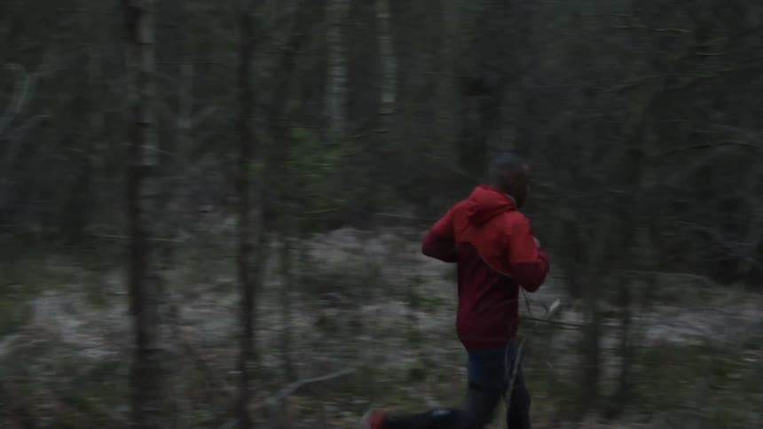 Man wearing shorts and a jacket jogs through forest