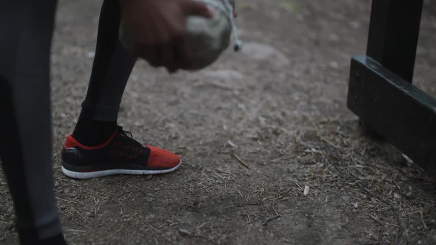 A person is standing outdoors and picking up a large rock