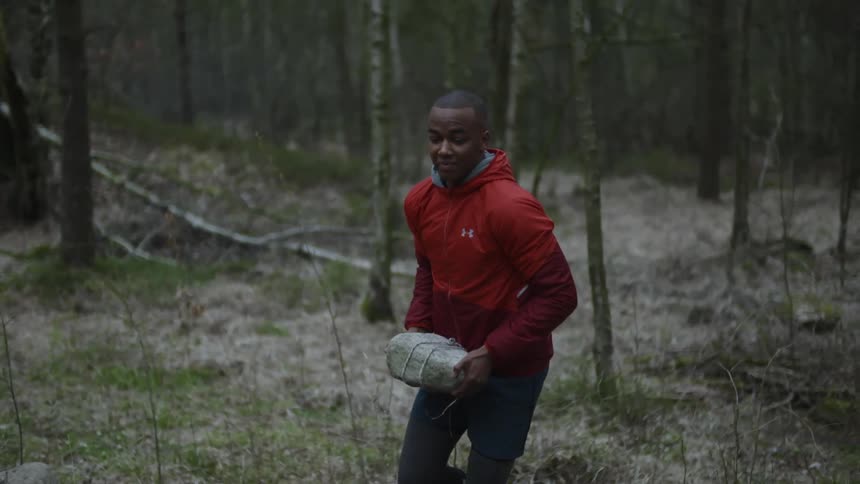 A man carries a large rock in the forest