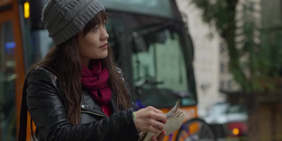 Woman stands near busy street as bus passes and looks through photographs