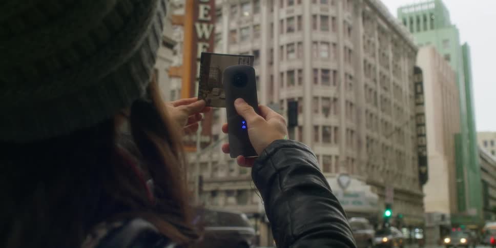 A woman is taking pictures of a downtown city during midday