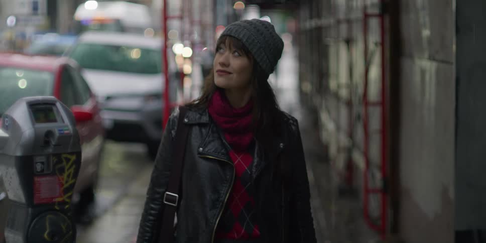 A woman wearing a grey beanie walking down a city sidewalk in the rain