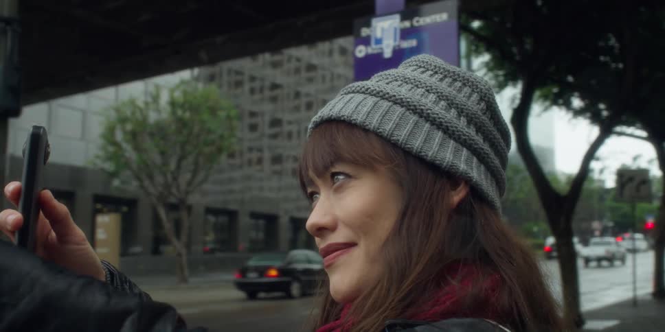 Woman stands at intersection smiling as she compares building to photograph