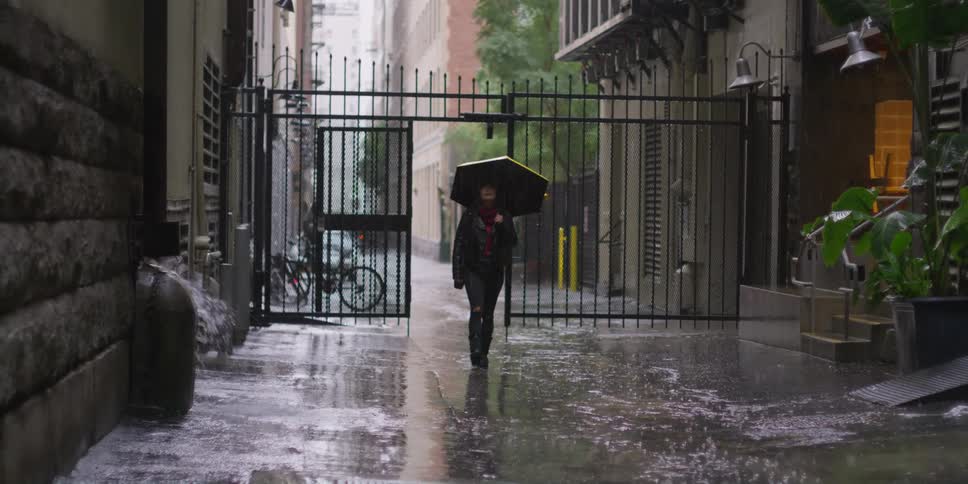 A woman with an umbrella is walking in the rain in an alley between buildings