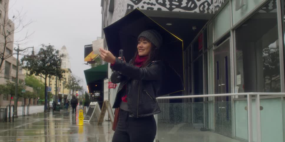 Woman stands on wet sidewalk comparing photograph to site