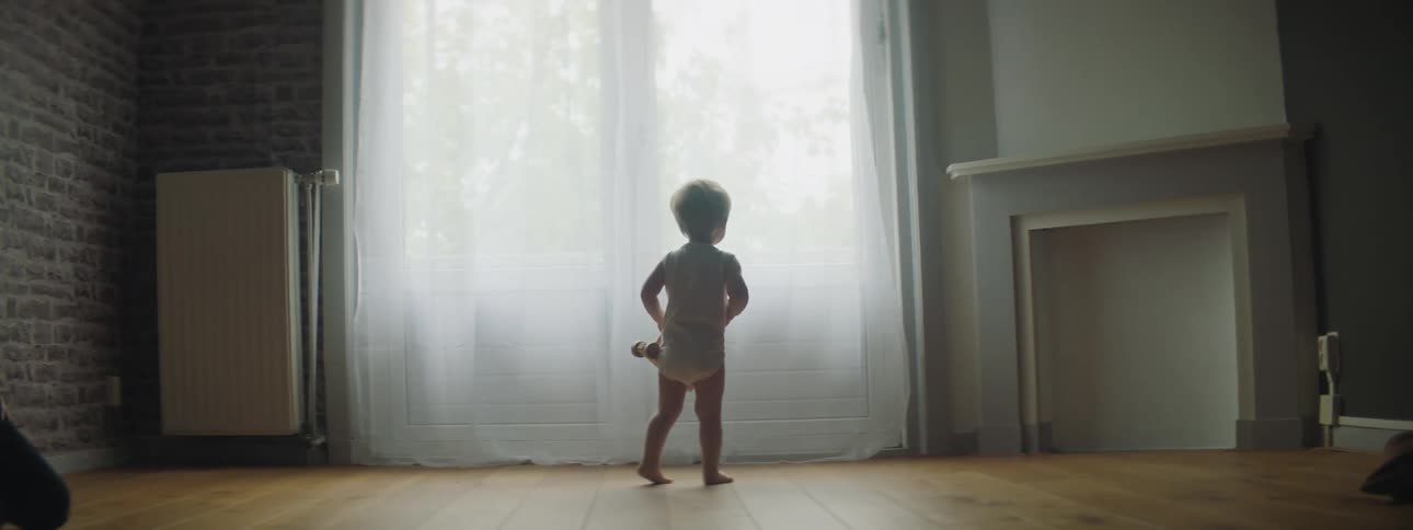 Toddler boy looks out the windows and wanders around in a room