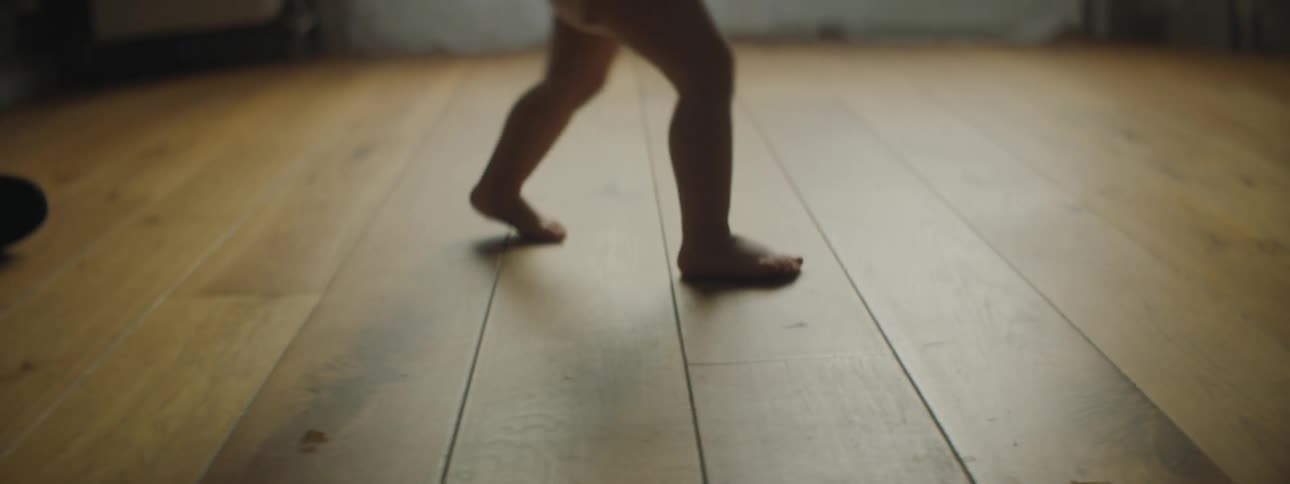 A barefoot baby playing with a toy car on a wood floor indoors
