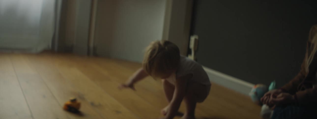 A toddler rolls a play car across the floor at home