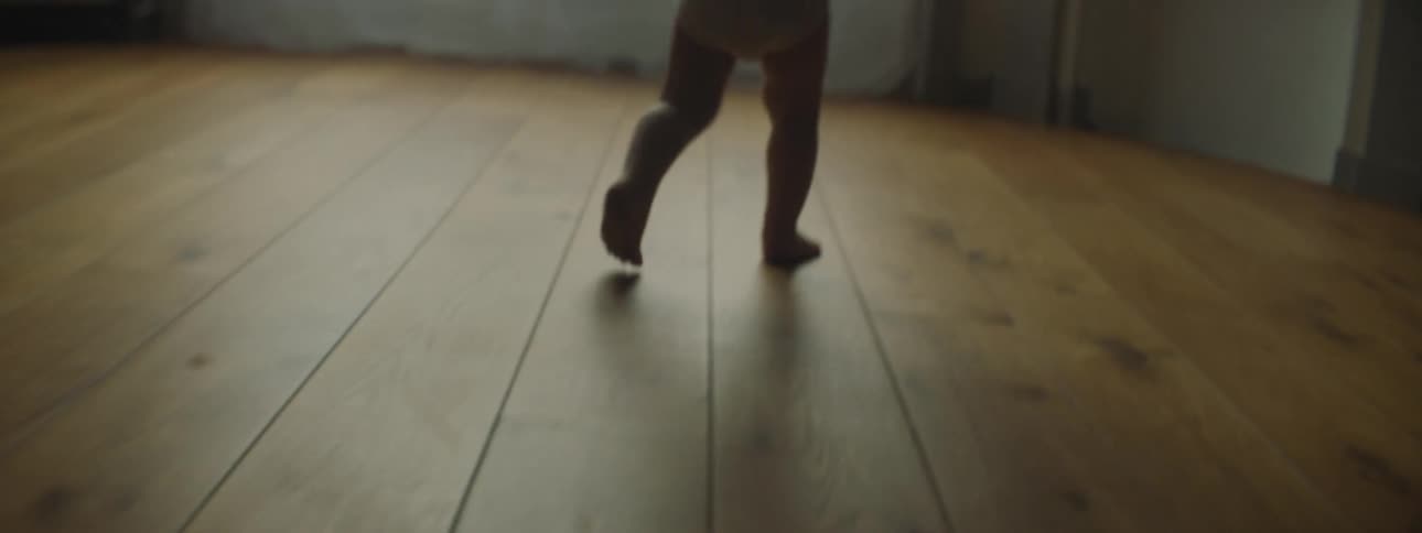 A baby in a room walking towards a fireplace and a window with curtains
