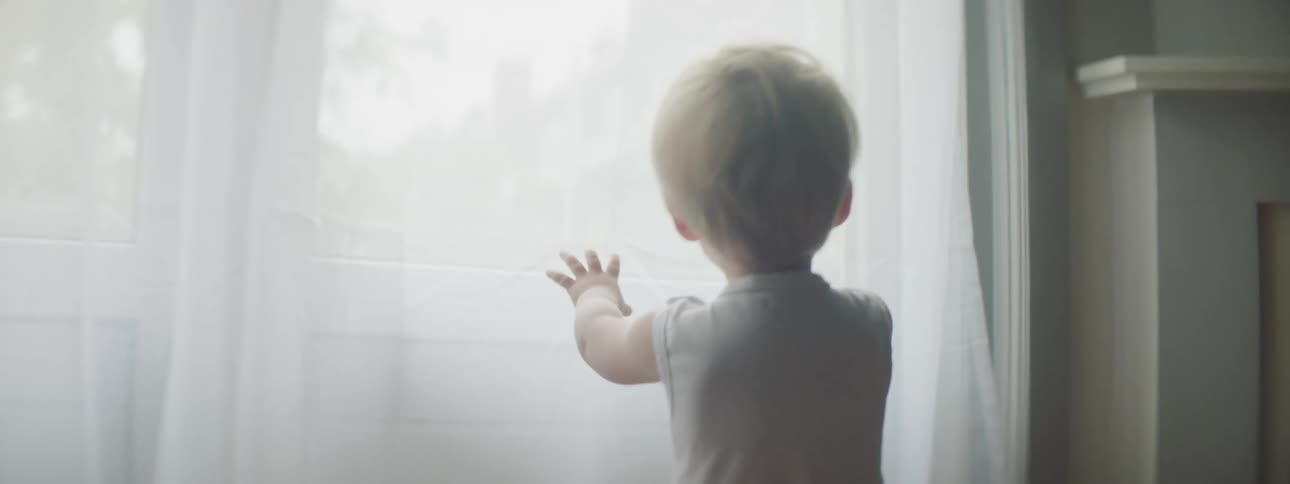 Blonde toddler walks toward window near mantle and touches curtain and sil