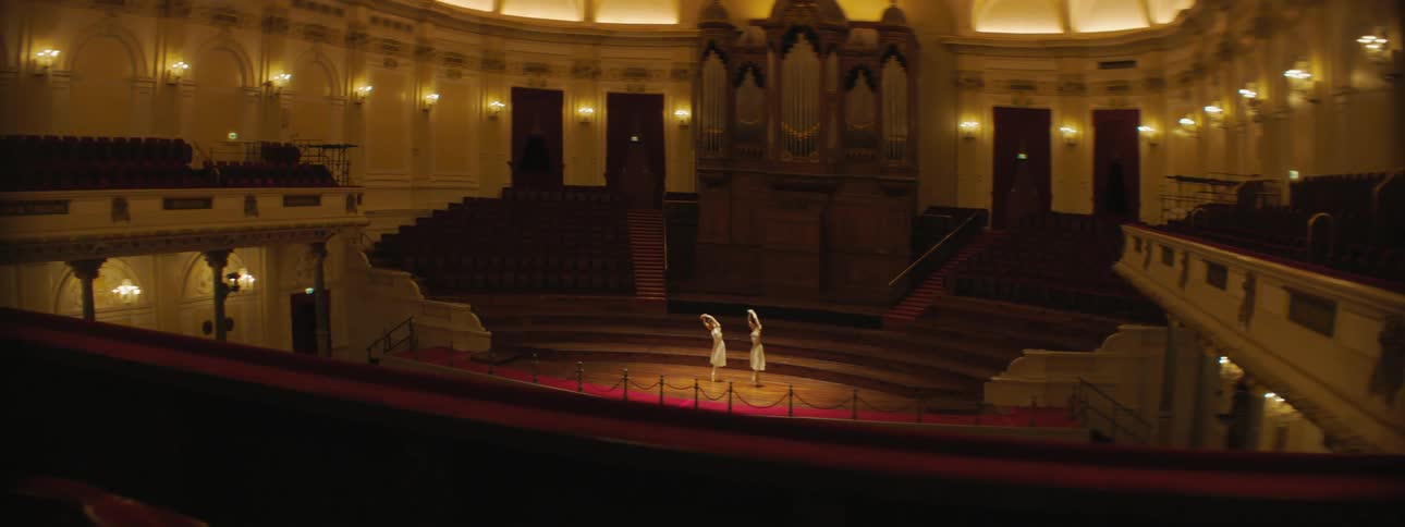 A pair of female dancers dance on the stage of an otherwise empty theater