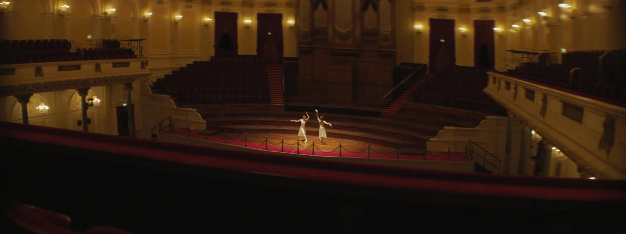 Two ballerinas dance on a stage in an empty auditorium