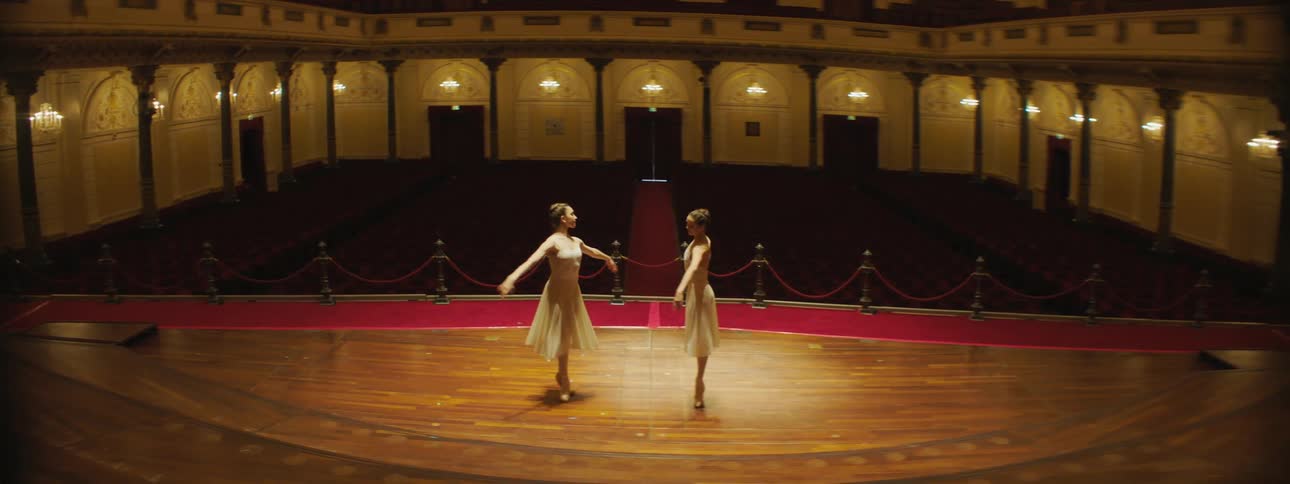 Two ballerinas dance together on a lit stage
