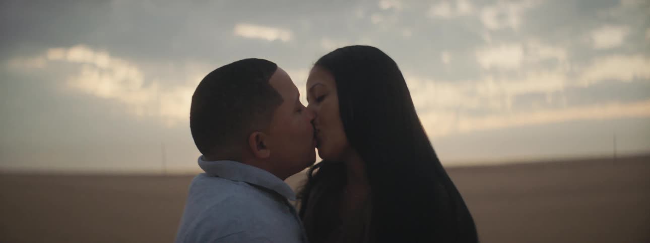 A man and woman kiss in a vast open field in the countryside