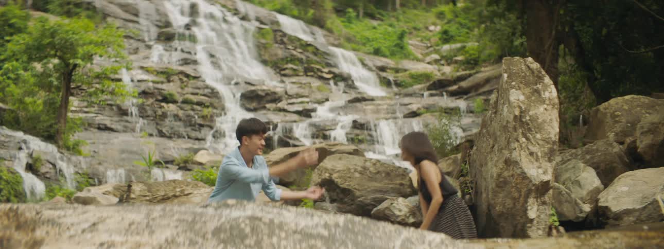 Young man and woman play in water at base of waterfall