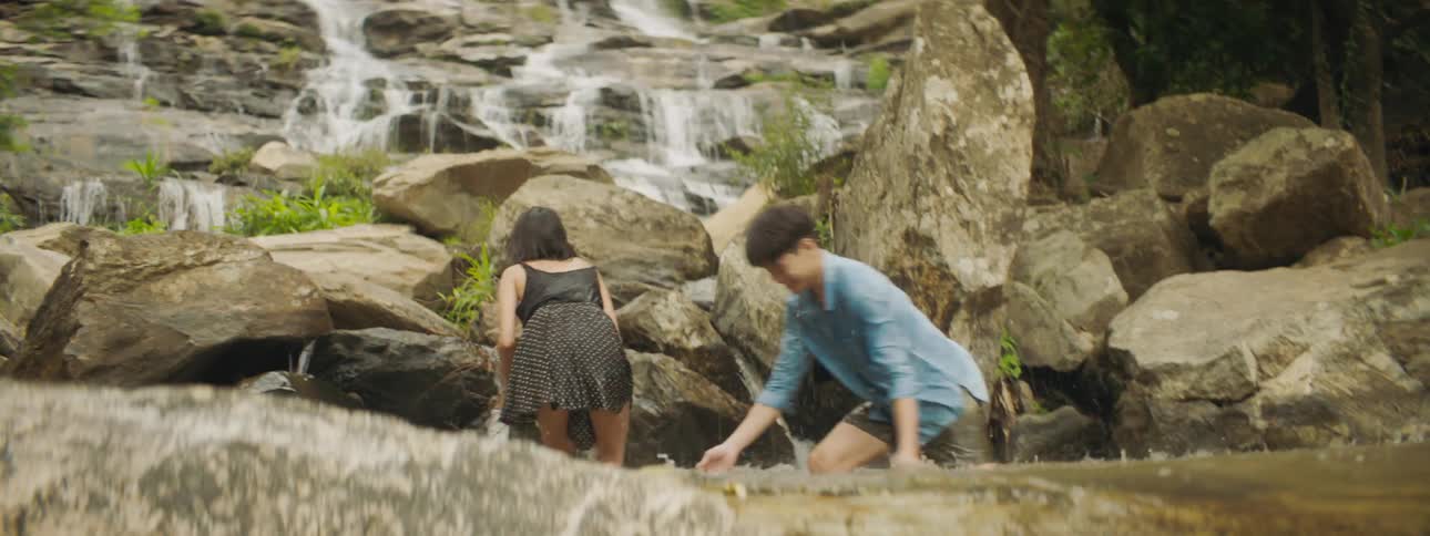 Two people splash water on each other playing in pool at base of waterfall
