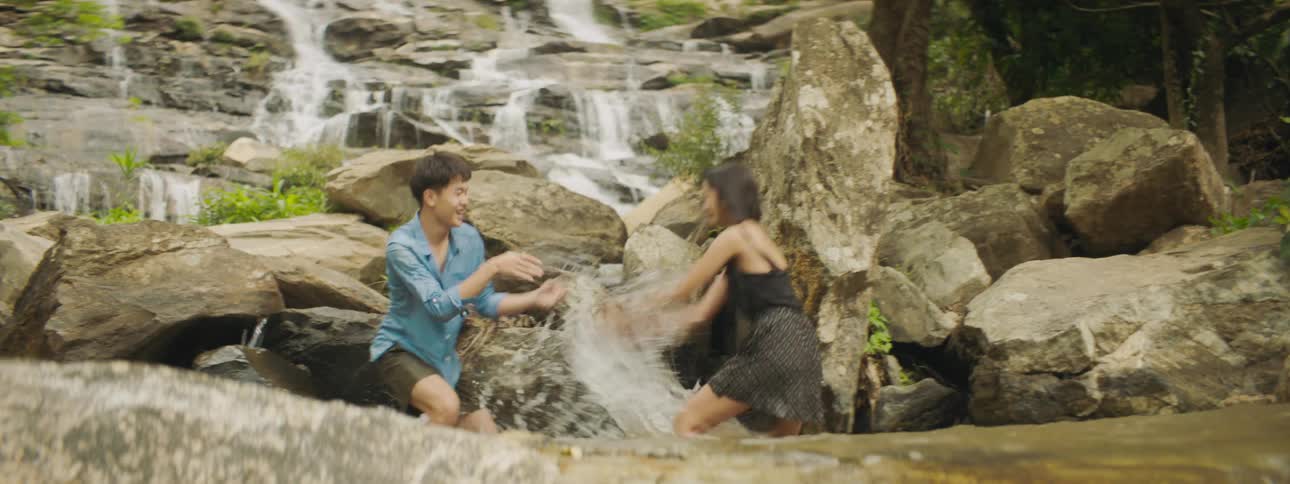 A girl and boy splash each other in the water pool of a mountainside waterfall