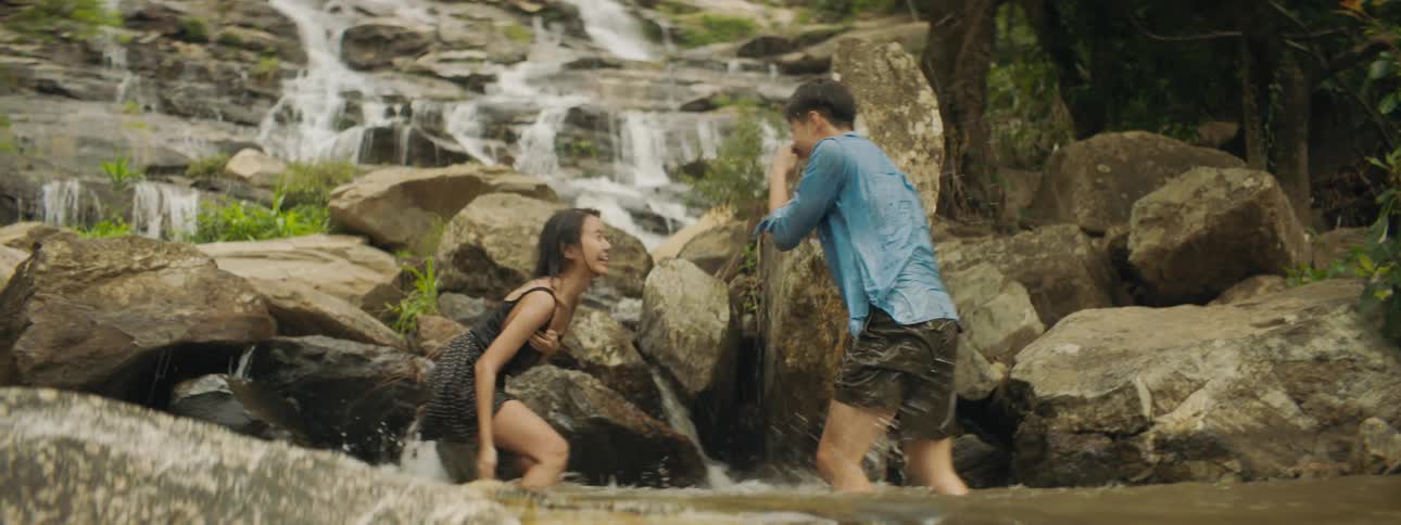 Two people play in water at base of waterfall splashing each other