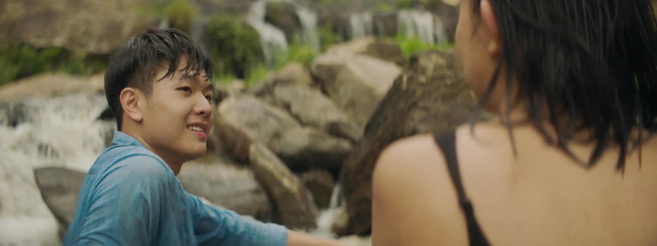 A man and a woman sitting and talking with a waterfall a river and a cliff in the background