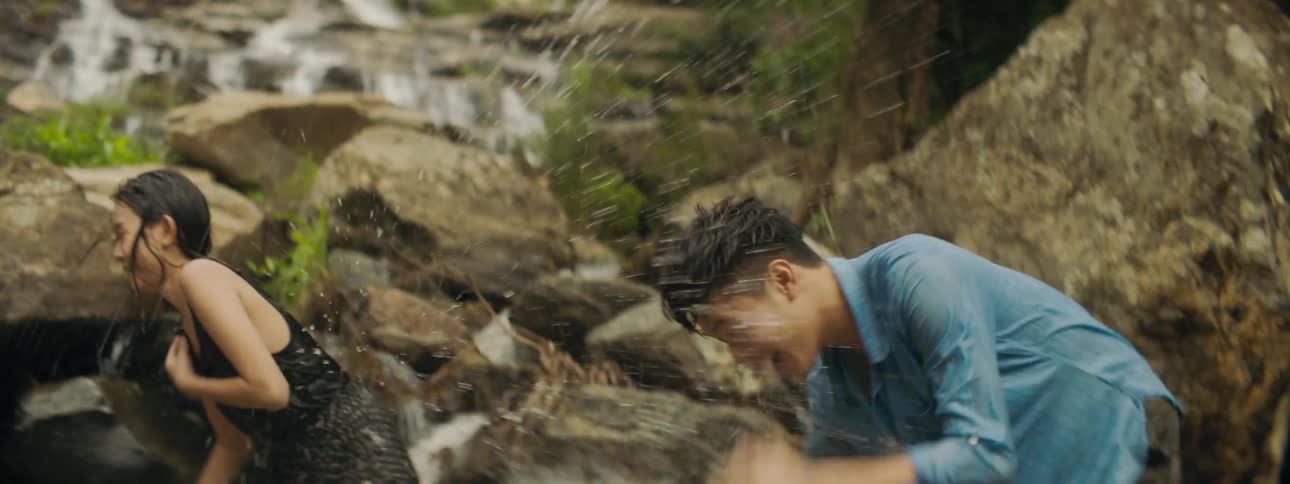 A man and woman standing in a stream splash each other with water