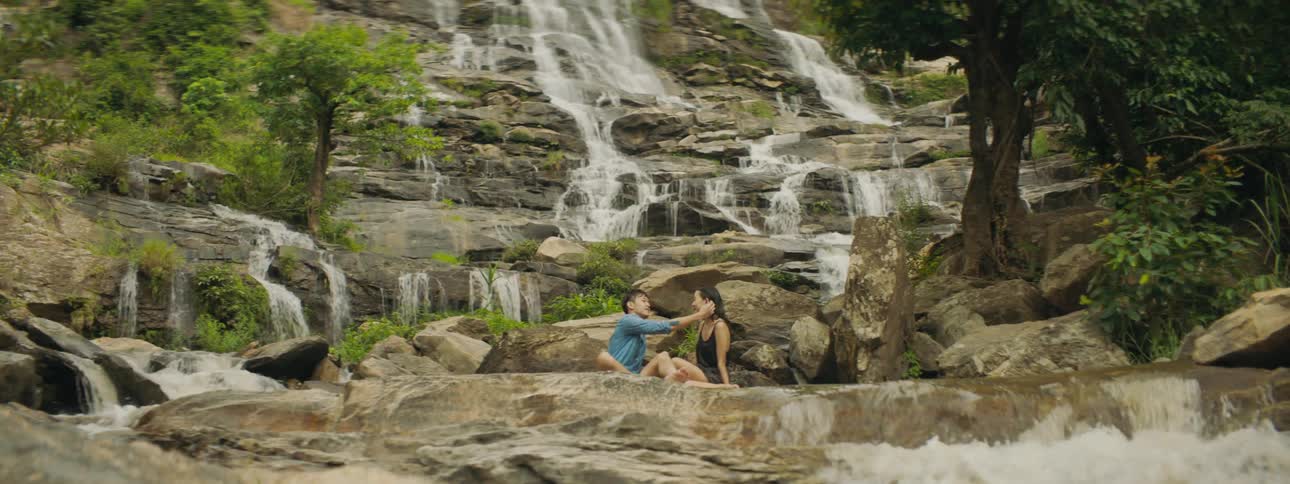 Couple relaxes in pool formed at base of waterfalls near rocks