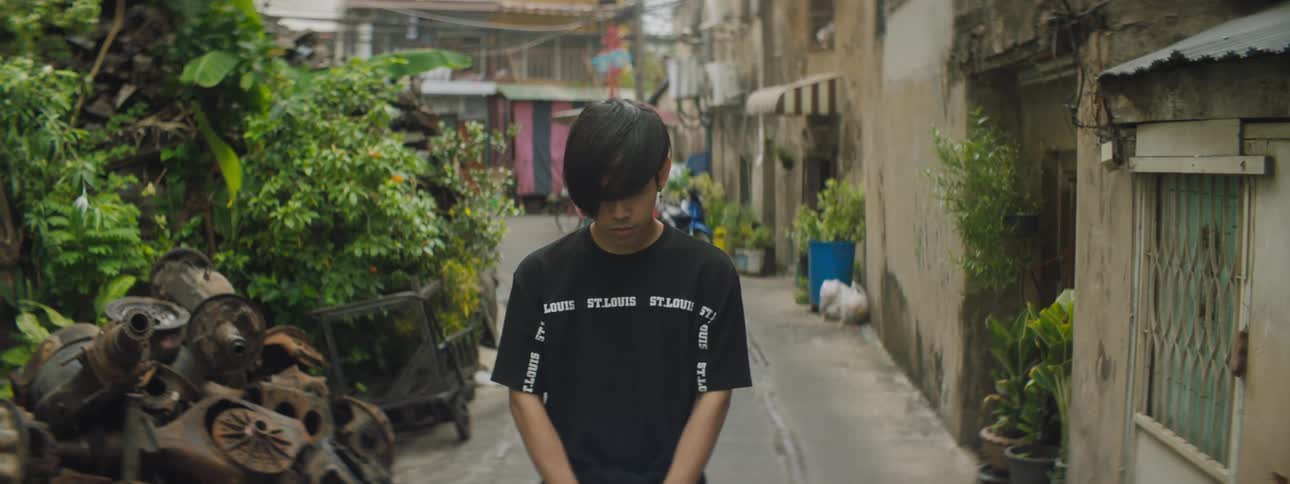 A boy standing in an alley with plants and buildings in the background
