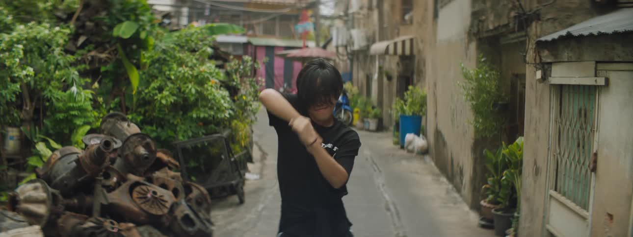 Male dancer performs routine in narrow alley next to building housing shops and homes