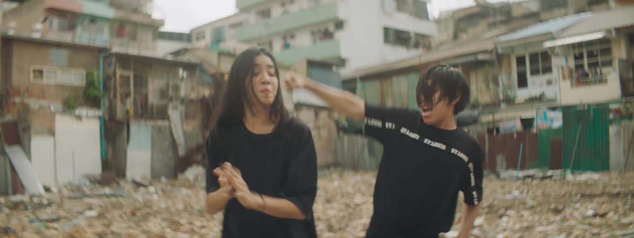 A boy and a girl dancing with buildings the sky and clouds in the background