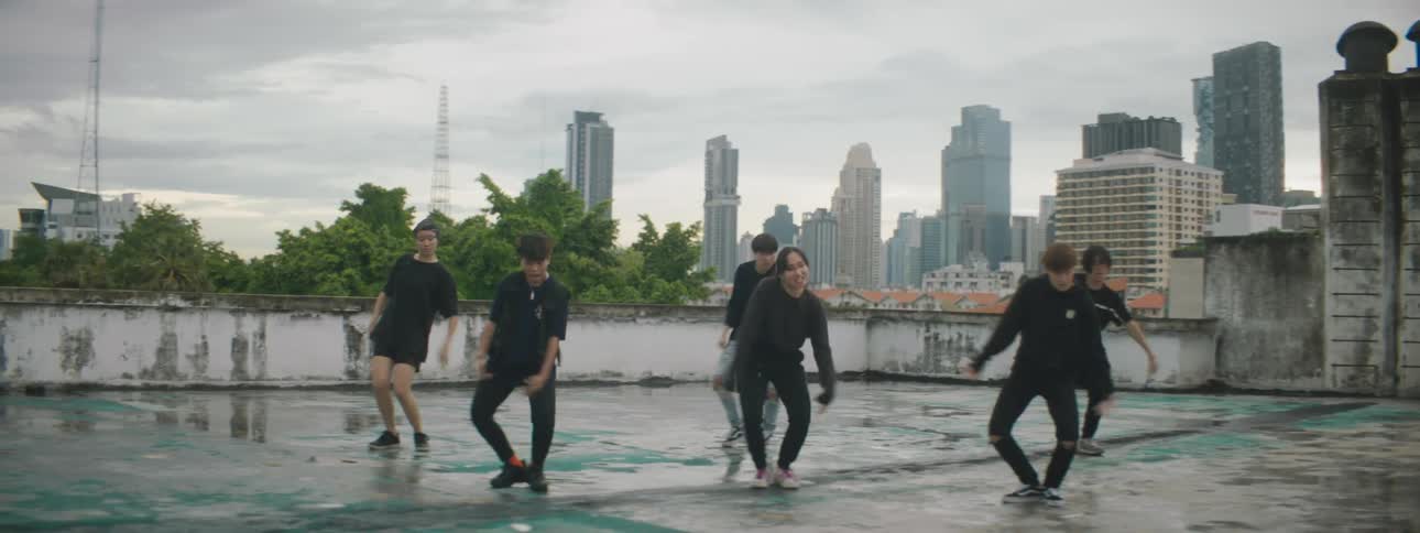A group of young adult performers dance on a city rooftop