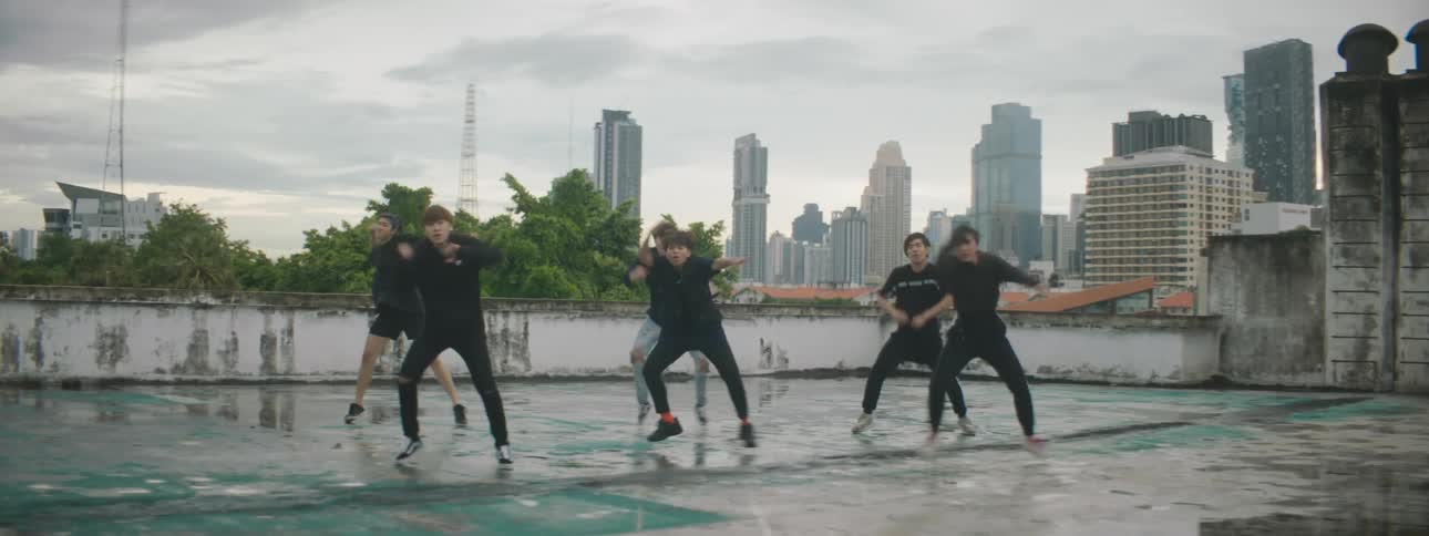 Men and women on a rooftop dancing with buildings the sky and clouds in the background