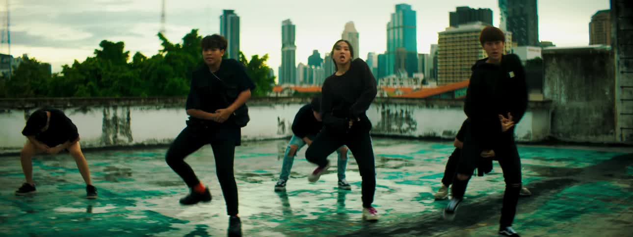 A group of teenagers dance on a rooftop with the city skyline in the background
