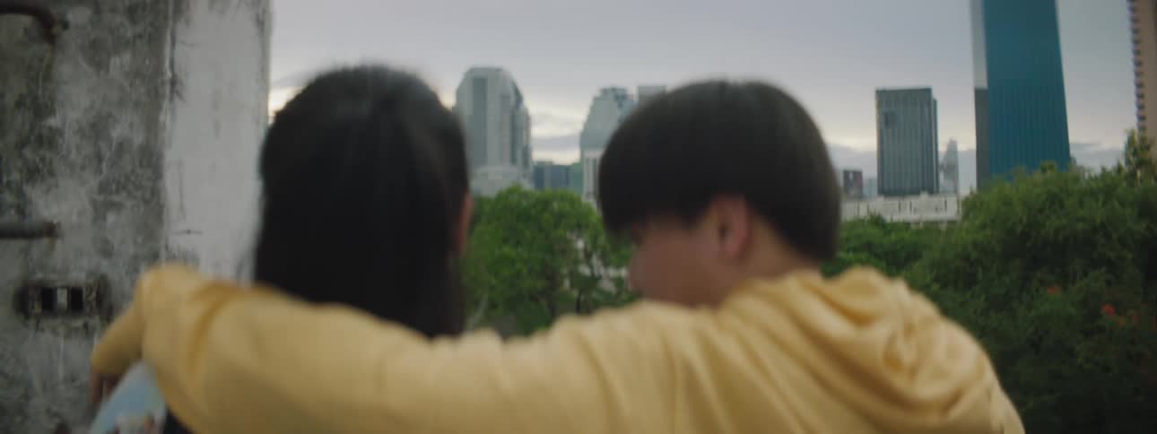 A man and a woman hugging with buildings the sky and clouds in the background